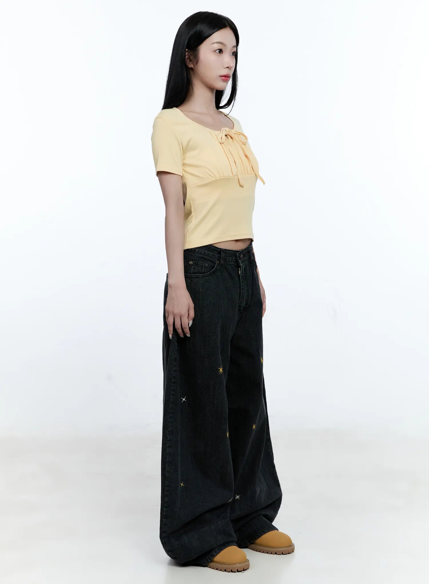 Wynter Star Embroidered Denim Jeans CG507 in black, side view on model, relaxed wide-leg silhouette with star embroidery, paired with yellow bow crop top and tan chunky shoes.