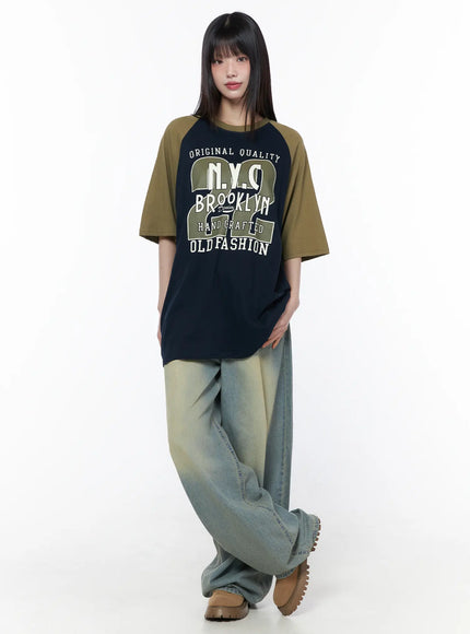 Rain Vintage Washed Wide Leg Jeans CU519 in light blue, front full-body on model, vintage washed yellow-tint denim, styled with navy-olive raglan graphic tee and brown chunky boots.