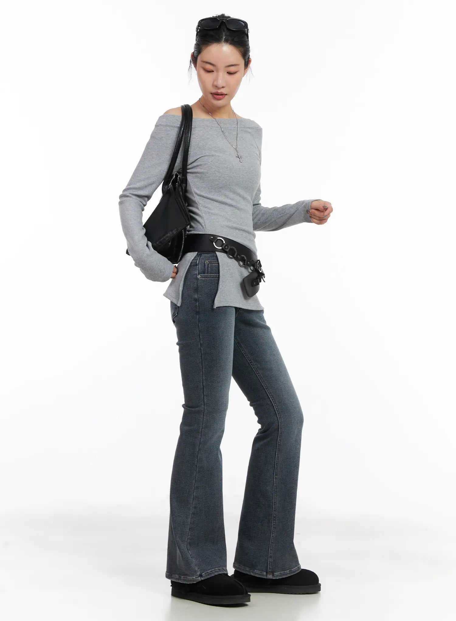 Kiera Low-Rise Fleece-Lined Bootcut Jeans CD509 in washed dark blue, three-quarter front-side view on model, bootcut silhouette, styled with grey off-shoulder top, black grommet belt, and shoulder bag.