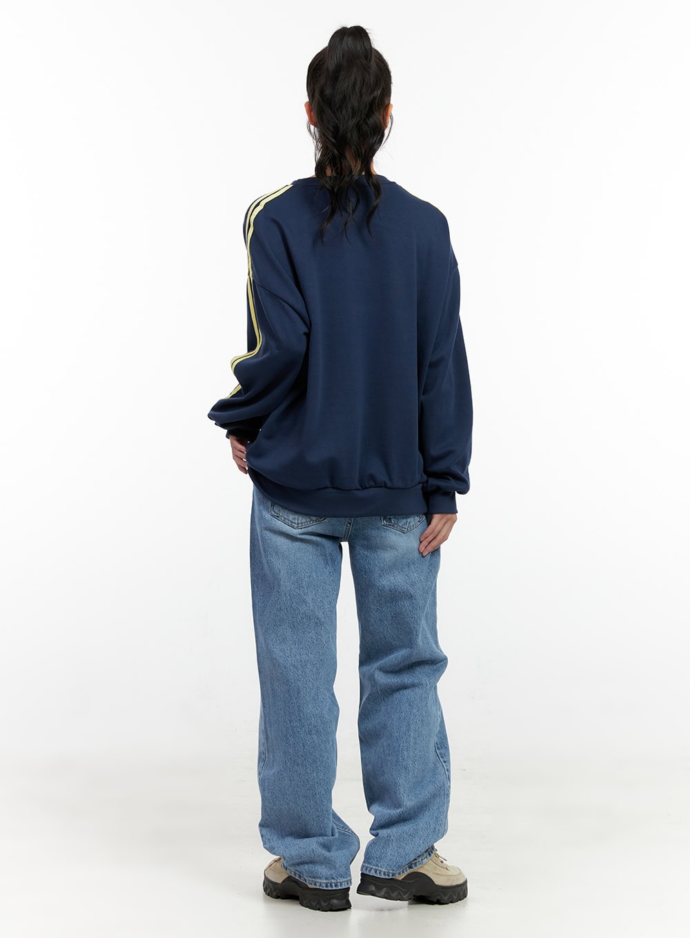 Carly Cloud Wide-Leg Jeans ON404 in blue, back full-body on model, wide-leg washed denim with rear five-pocket detail and relaxed fit, paired with navy varsity sweatshirt and chunky sneakers.