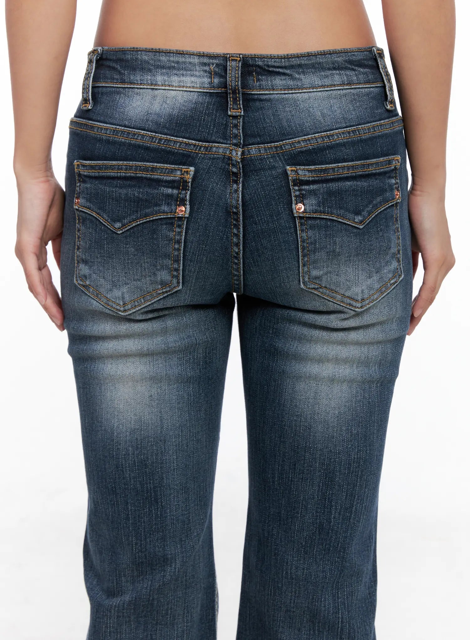 Saanvi Vintage Wash Flare Jeans CS522 in dark blue, close-up back view on model, curved back pockets with contrast topstitching and copper rivets, vintage wash fading detail on denim fabric.