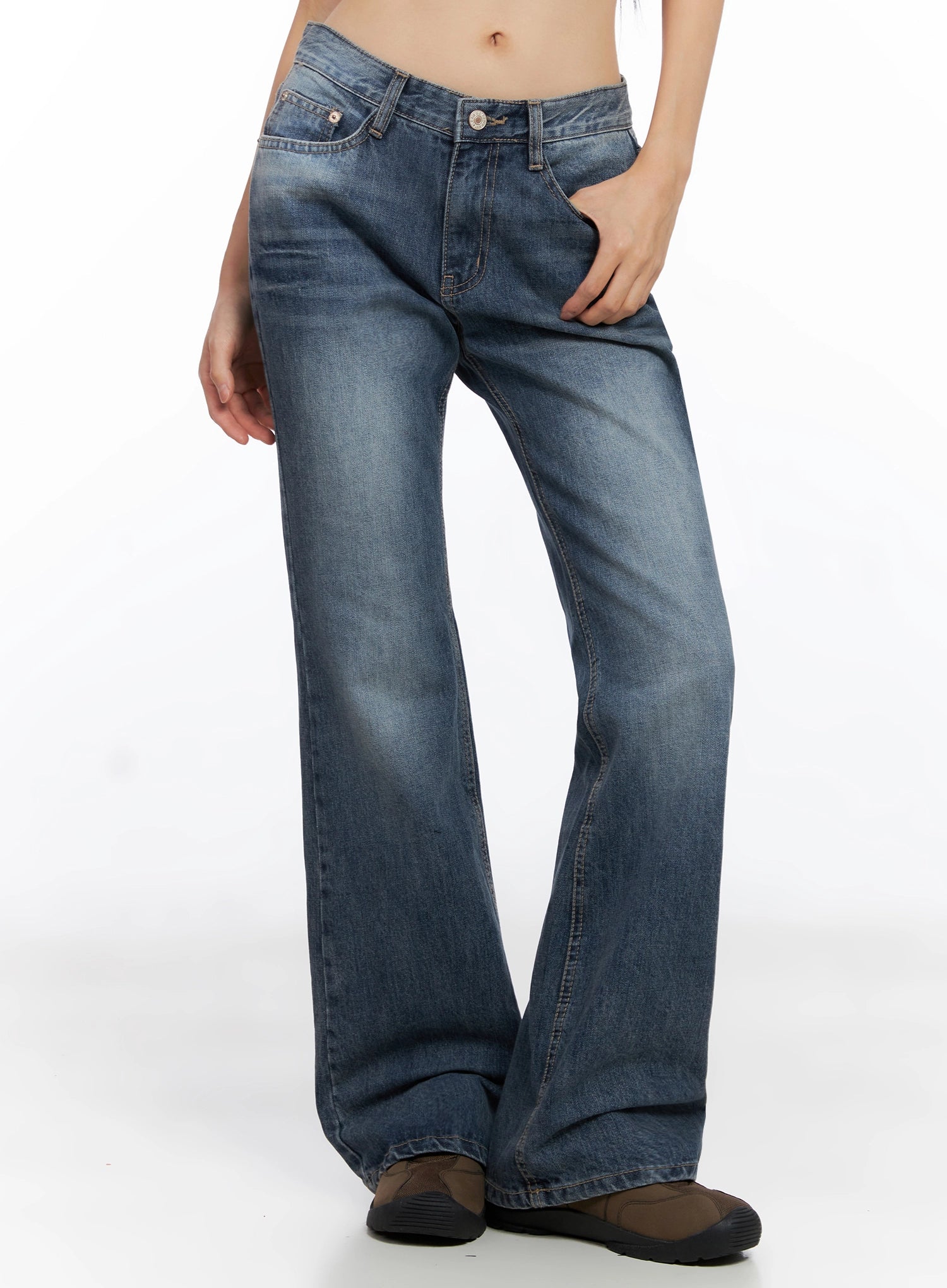 Myra Washed Bootcut Jeans IO516 in dark blue, angled front view on model, hand in pocket, low-rise cut with washed fading, flared bootcut hem pooling at brown shoes.