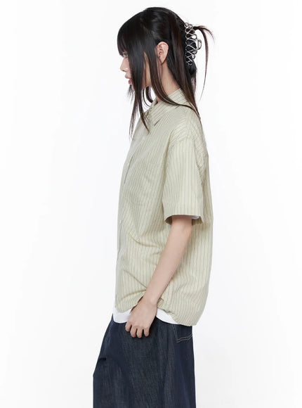 Oversized Short Sleeve Button-Up Shirt CU519 in light beige, close side view on model, striped lightweight fabric, dropped shoulder seam and straight hem visible, layered over white tee with dark wide-leg denim.