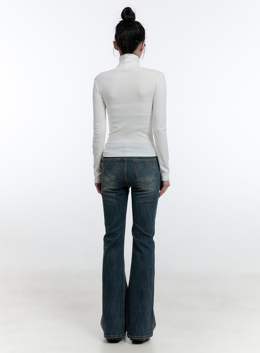Mallory Skinny Bootcut Jeans CJ520 in blue, full-body back shot on model, slim-fit washed denim with back pockets and wide bootcut hem, styled with white turtleneck.