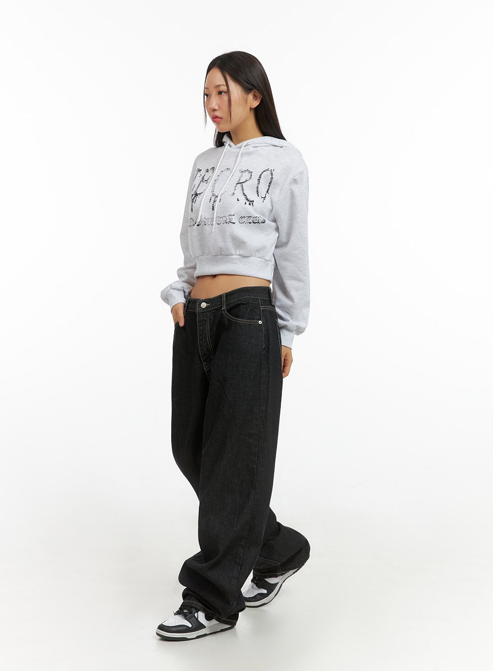 Clover Stitched Baggy Jeans IS402 in black, front 3/4 angle on model, low-rise wide-fit denim with visible coin button and contrast stitching, styled with crop hoodie and Jordan sneakers.