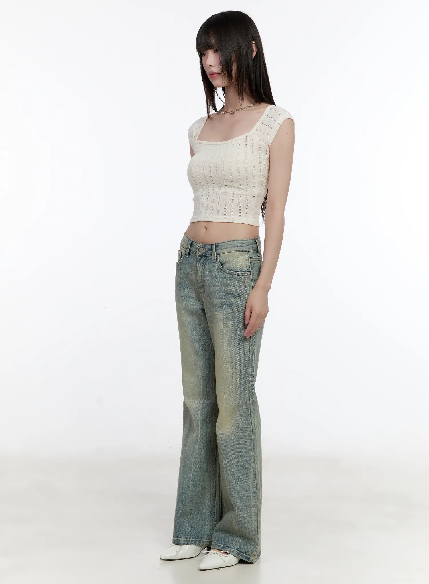 Roa Vintage Blue Flared Denim Jeans CL504 in blue, three-quarter side full-body shot on model looking right, washed flared denim with front pockets, cream knit crop top, white flats.
