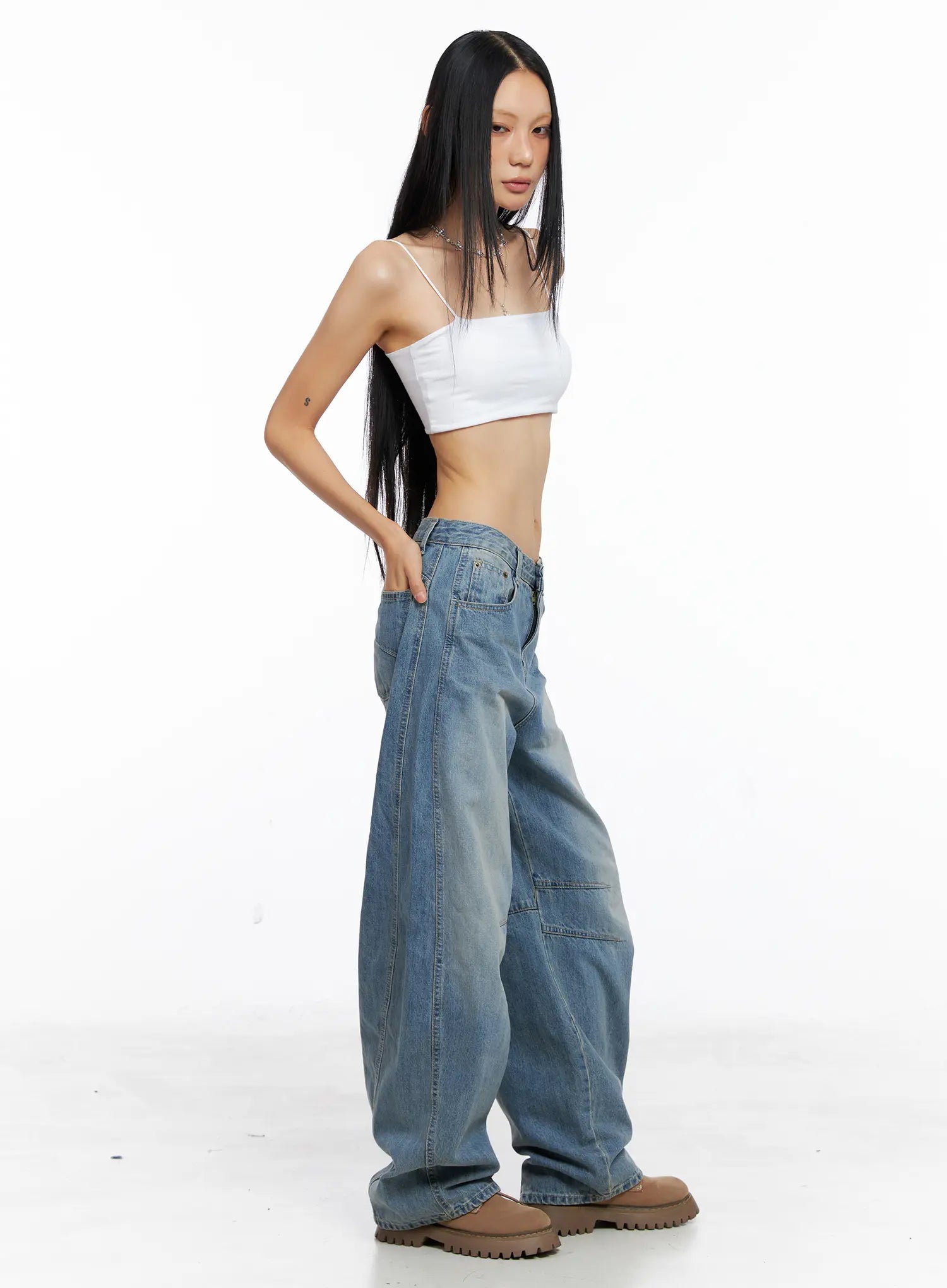 Dakota Relaxed Fit Vintage Wash Jeans CS511 in blue, side studio shot on model with hand in pocket, wide-leg low-rise cotton denim showing curved seam and patch knee detail, white cami and tan chunky boots.
