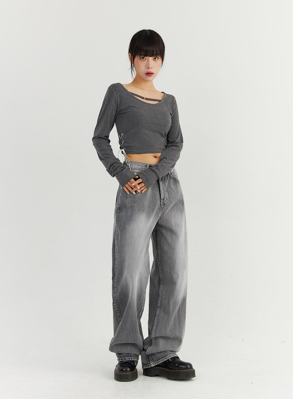 Grey Washed Wide Leg Jeans CO323 in Gray, full-body front view on model with hands clasped, low-rise wide-leg denim with lighter fade at thighs, styled with gray lace-up crop top and chunky boots.