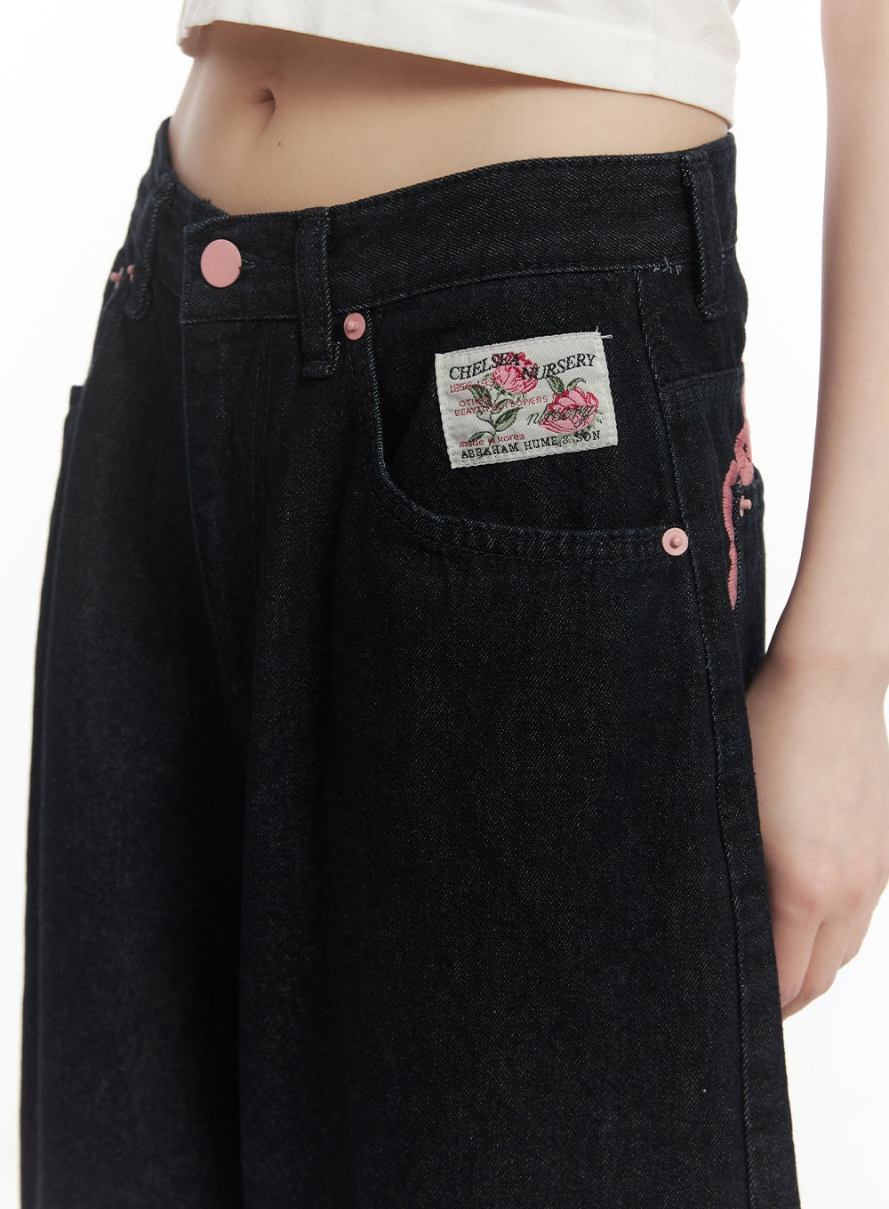 Dory Embroidered Baggy Jeans CF518 in dark blue, front waist close-up on model showing Chelsea Nursery patch label, pink rivet buttons, and rose embroidery detail.