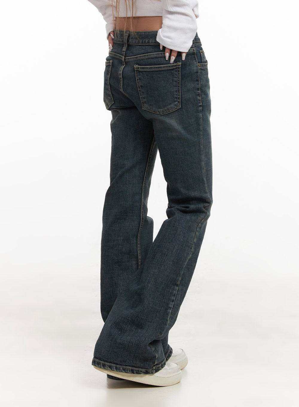 Natalia Low-Rise Flared Jeans CJ508 in dark blue, rear three-quarter close-up on model, washed denim highlighting back patch pocket and flared leg silhouette, styled with white ribbed top and white sneakers.