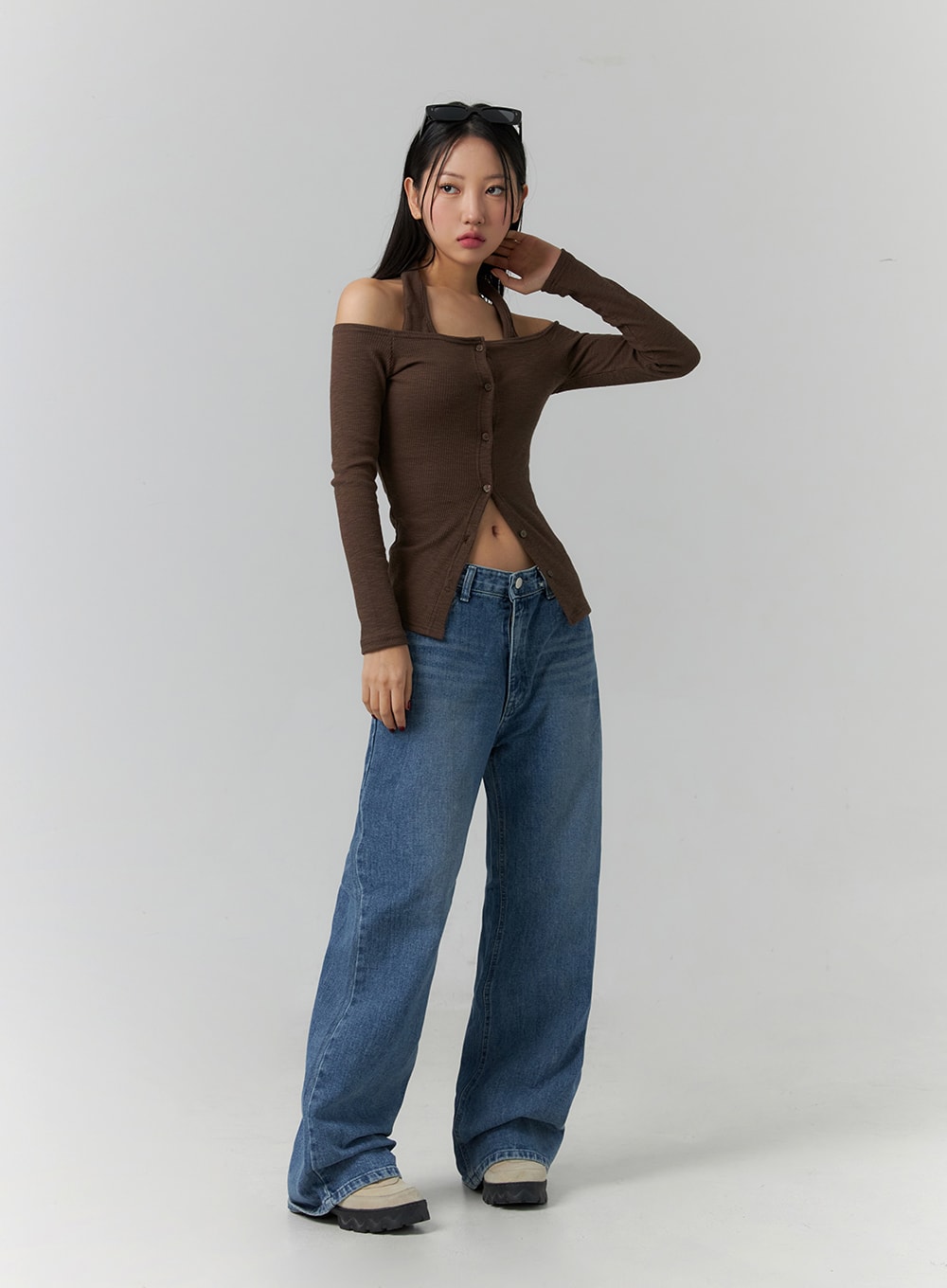 Wide Leg Jeans J12 in blue, three-quarter front angle on model with hand raised to face, wide-fit cotton denim with gradation wash, long leg pooling at ankle, styled with brown off-shoulder top.