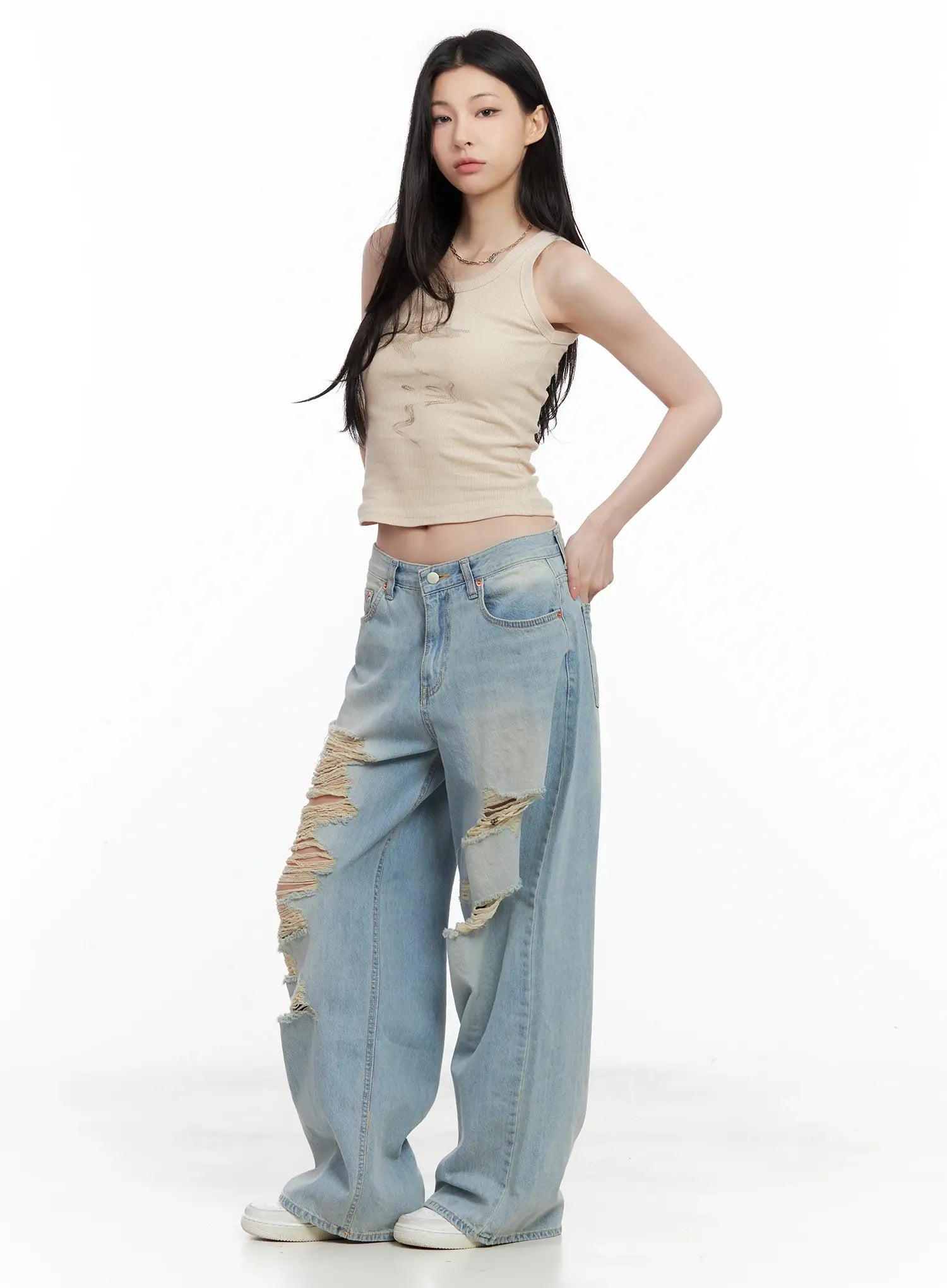 Gyuri Dirty-Wash Distressed Wide Jeans CU530 in blue, three-quarter front on model, low-rise wide fit, hand on hip, distressed thigh rips, beige crop tank, white sneakers.