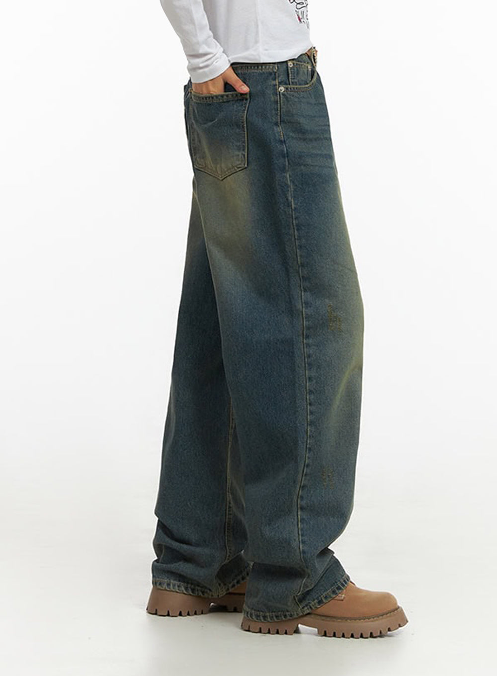 Anya Wide Fit Denim Jeans IO409 in blue, side view on model, wide-leg washed denim showing roomy silhouette, back pocket and side seam detail visible, hand in pocket, paired with graphic long-sleeve.