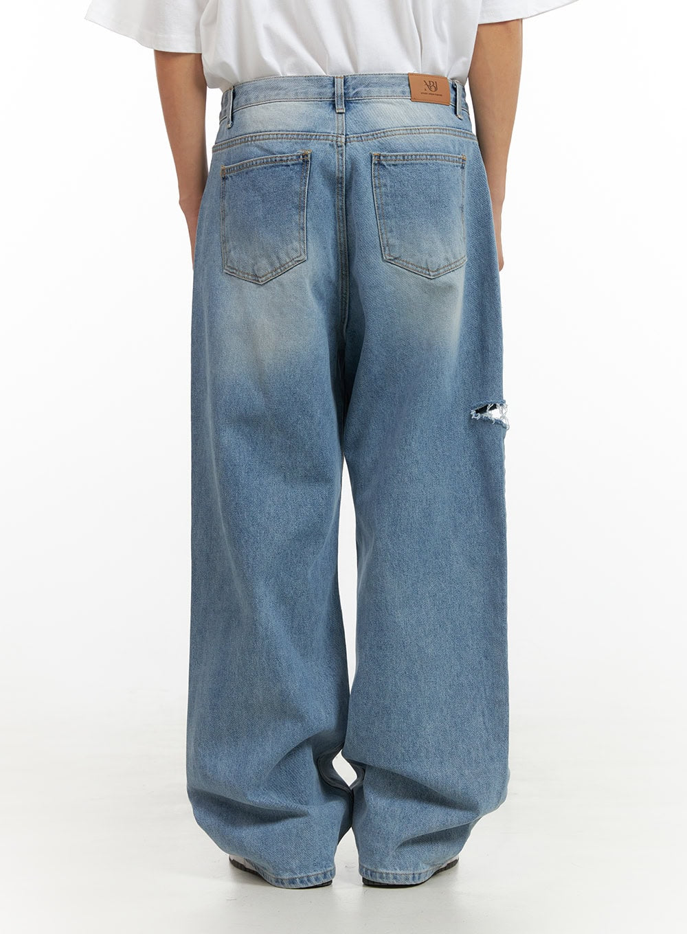 Men's Cut Out Baggy Jeans IU419 in blue, back view on model, two back pockets with leather brand patch at waistband, knee-area cut-out visible on left leg, wide baggy fit.