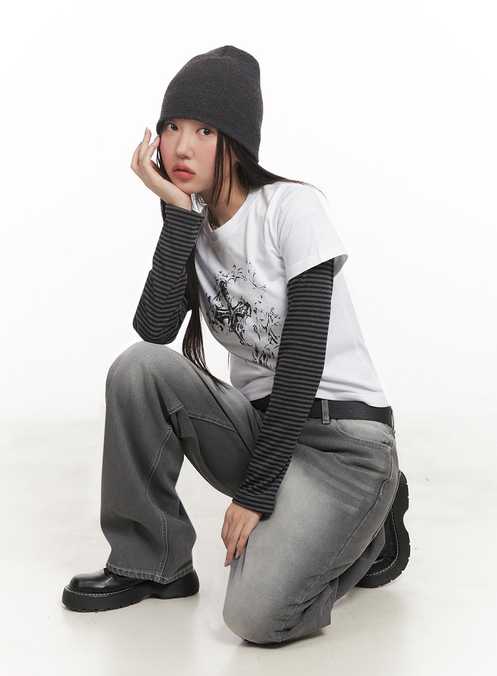 Becca Washed Straight-Leg Jeans IM524 in grey, crouching editorial pose on model, wide-fit washed denim showing volume at thigh, styled with beanie, striped top, and belt.