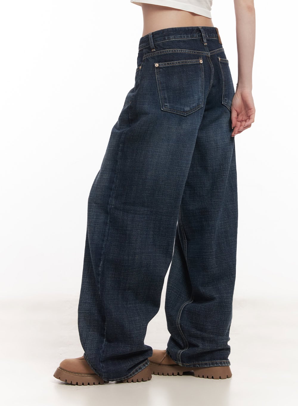 Annie Washed Wide-Leg Jeans CM518 in dark blue, angled side close-up on model, washed cotton denim with back pocket detail, low-rise waistband and voluminous wide leg, white crop top.
