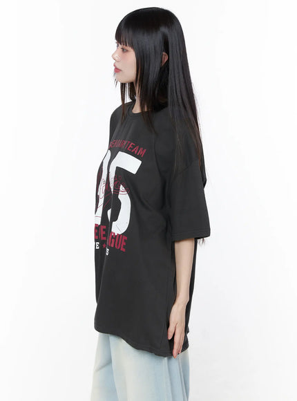 Oversized Graphic Tee CU519 in dark gray, side close-up on model, highlighting the oversized boxy silhouette, dropped shoulder seam, and 95 graphic wrapping around the torso, with light jeans.