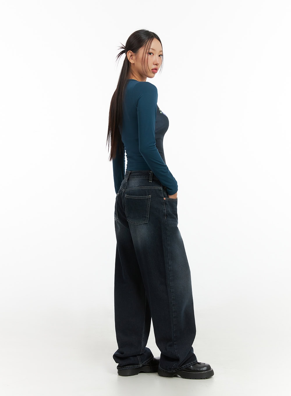 Evelyn Washed Baggy Jeans (Dark Blue) IS402 in dark blue, back three-quarter view on model looking over shoulder, wide baggy washed denim with patch pockets, styled with teal long-sleeve top.