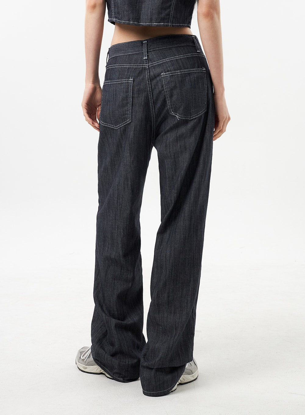Low Rise Wide Pants CU312 in dark grey, back mid-shot close-up on model, back yoke with contrast white stitching and two rear patch pockets, wide-leg hem at sneakers.