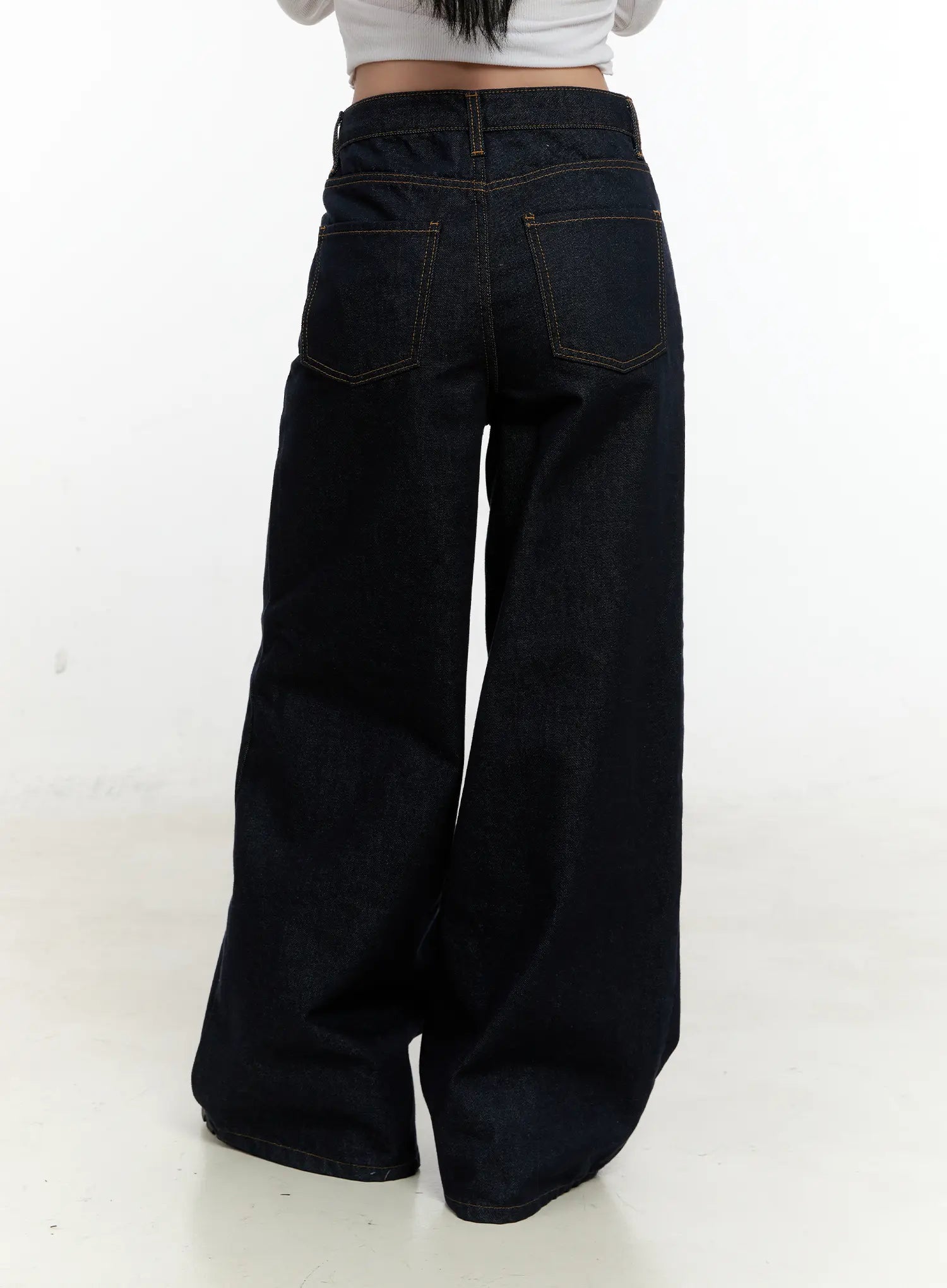 Nala Wide-Leg Bootcut Jeans CN506 in dark blue, back close-up cropped at waist on model, dual angled back pockets with contrast gold stitching, wide-leg hem spread on floor.