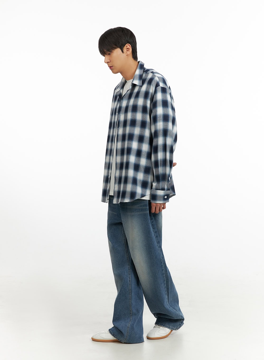 Men's Solid Baggy Jeans IU419 in blue, side full-length on model looking down, wide-leg washed denim with light fading, layered with plaid shirt over white tee.