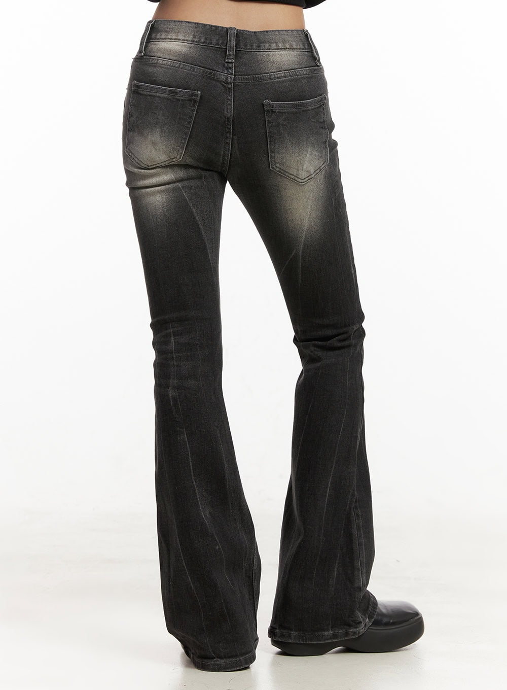 Georgina Low-Rise Flared Jeans CJ507 in black, back close-up on model, washed denim showing faded highlights on seat and thighs, two back patch pockets, dramatic flared hem with floor-grazing length.