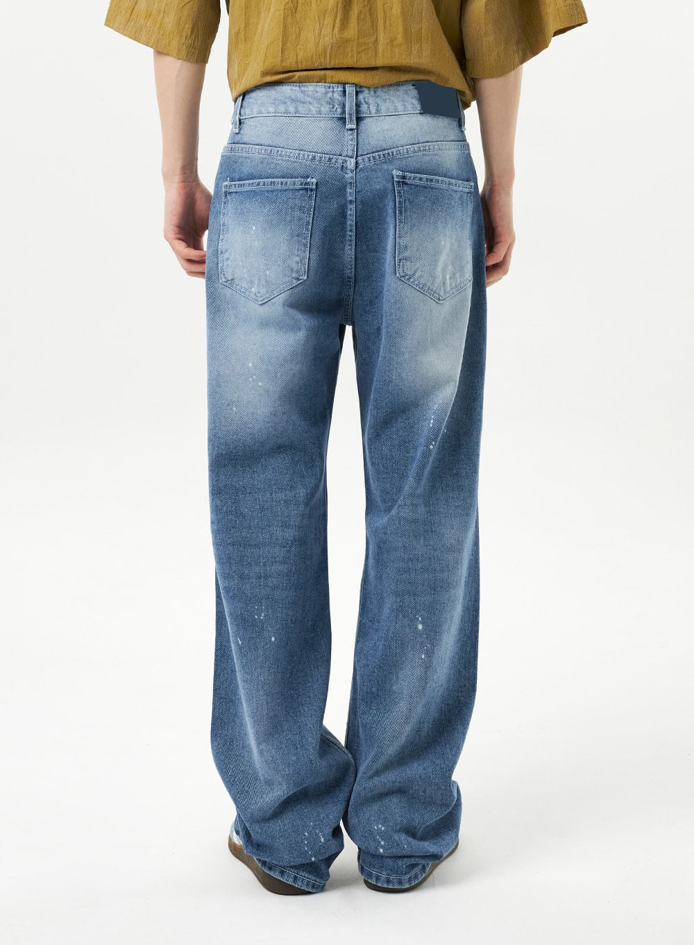 Ripped Jeans Unisex CU315 in mid blue, back view close-up on model, wide-fit denim showing dual back pockets, faded wash, and paint splatter across the leg, clean unripped reverse panel.