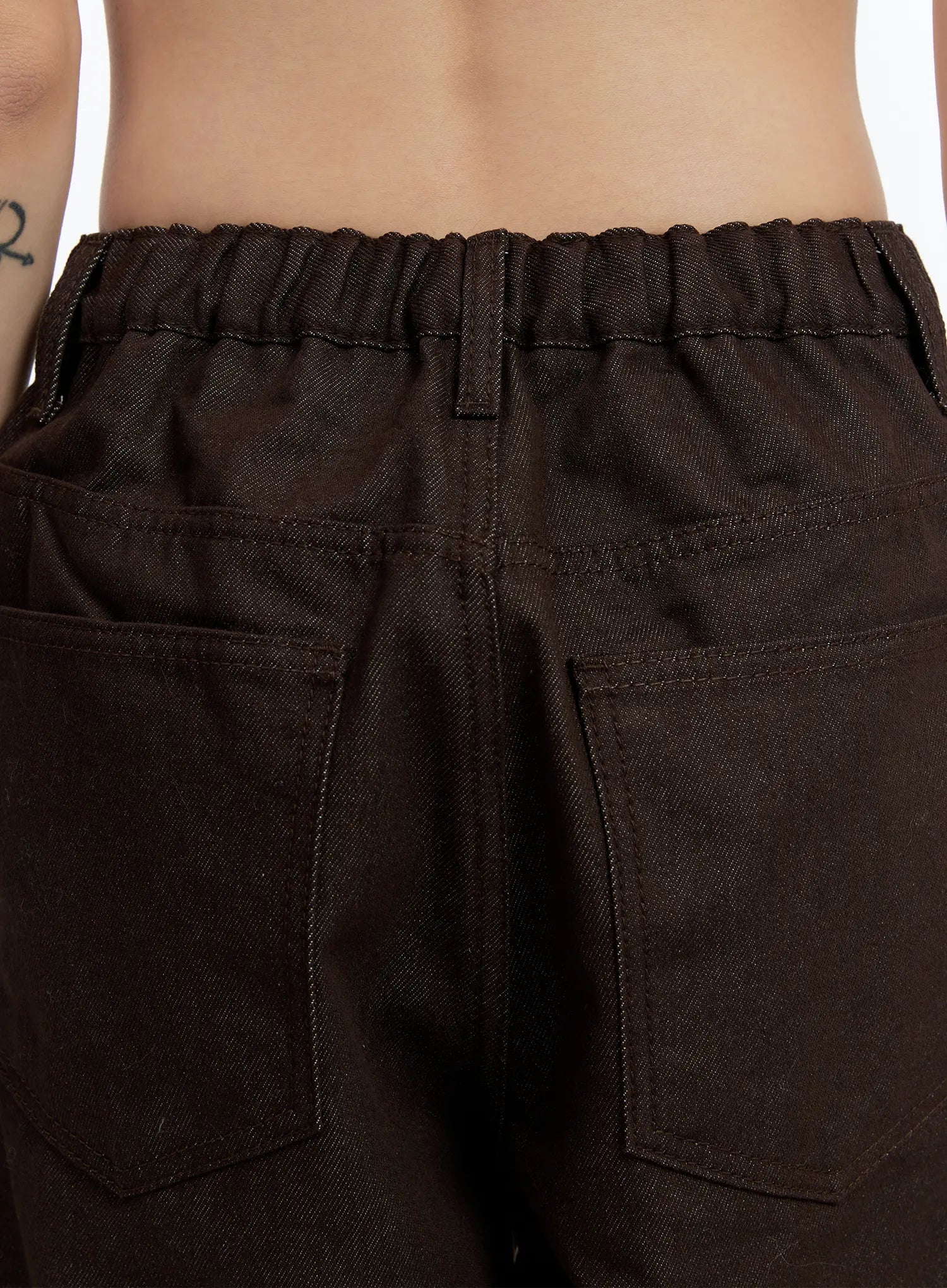 Emely Wide Leg Jeans CN524 in dark brown, back waistband close-up on model, elasticated banded waist detail with patch back pockets and visible topstitching on dark denim.