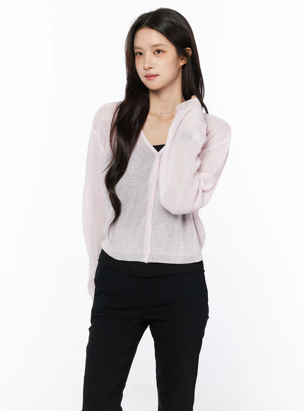 Sheer V-Neck Cardigan CU522 in pink, three-quarter front view on model, sheer open-knit fabric with V-neck and button front, layered over black bralette and black pants.