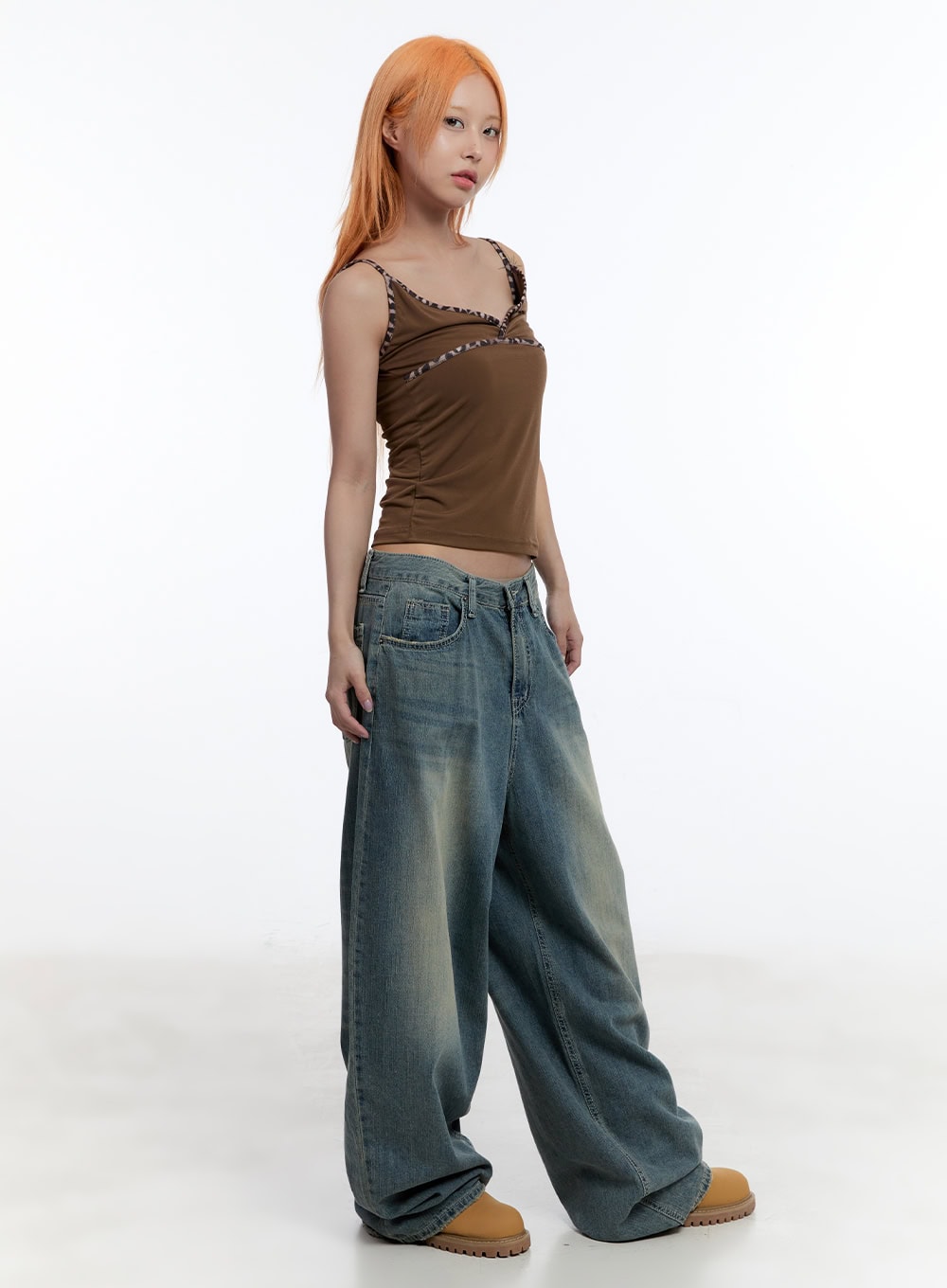 Jenna Relaxed-Fit Wide-Leg Jeans CU502 in blue, three-quarter side on model, washed fading detail across wide-leg thigh, low-rise waist, styled with brown cami and tan chunky boots.