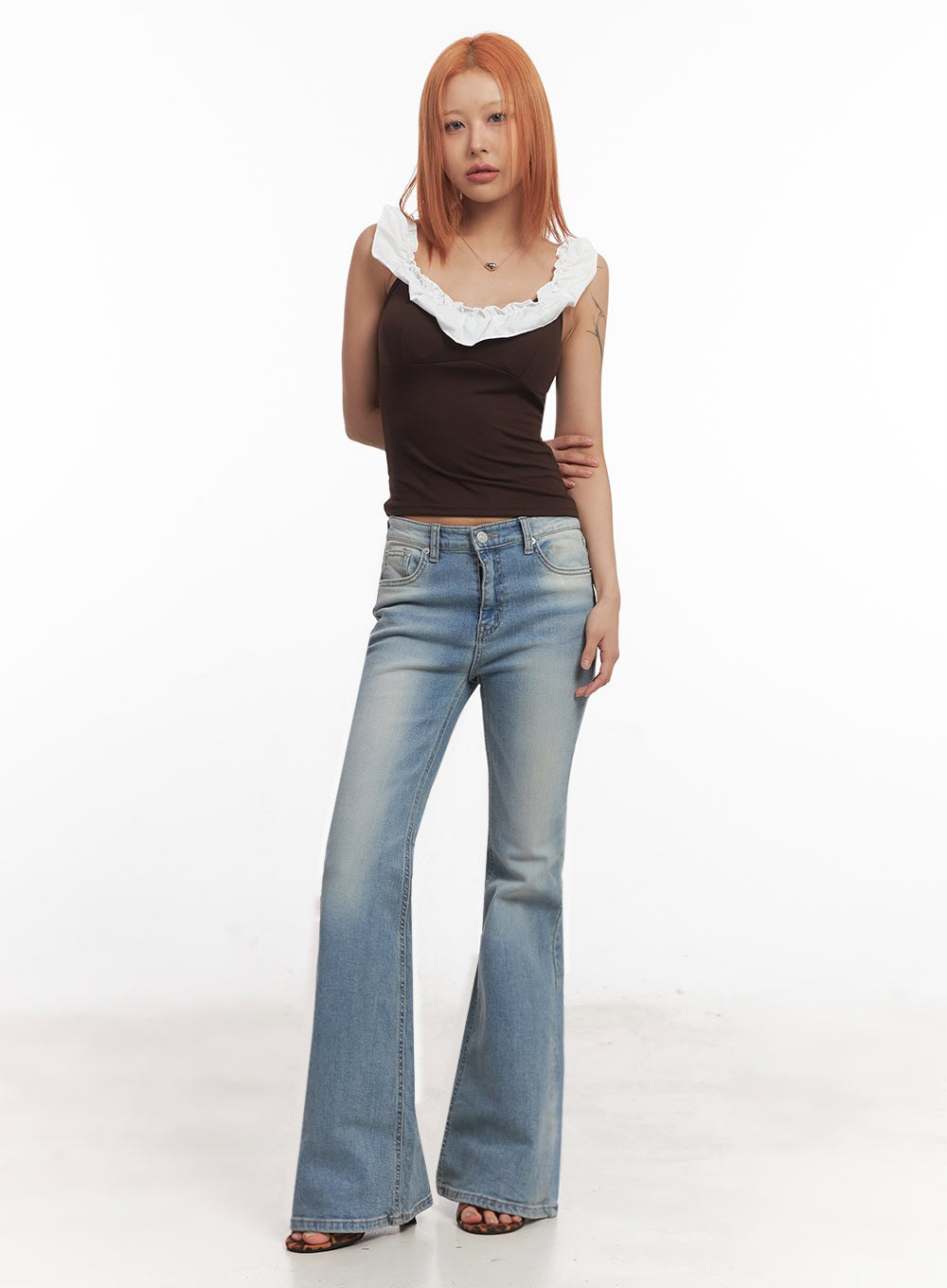 May Washed Flared Jeans IA515 in light blue, three-quarter front view on model with slight turn, slim fit through thigh flaring at hem, washed denim, paired with brown ruffle crop top.