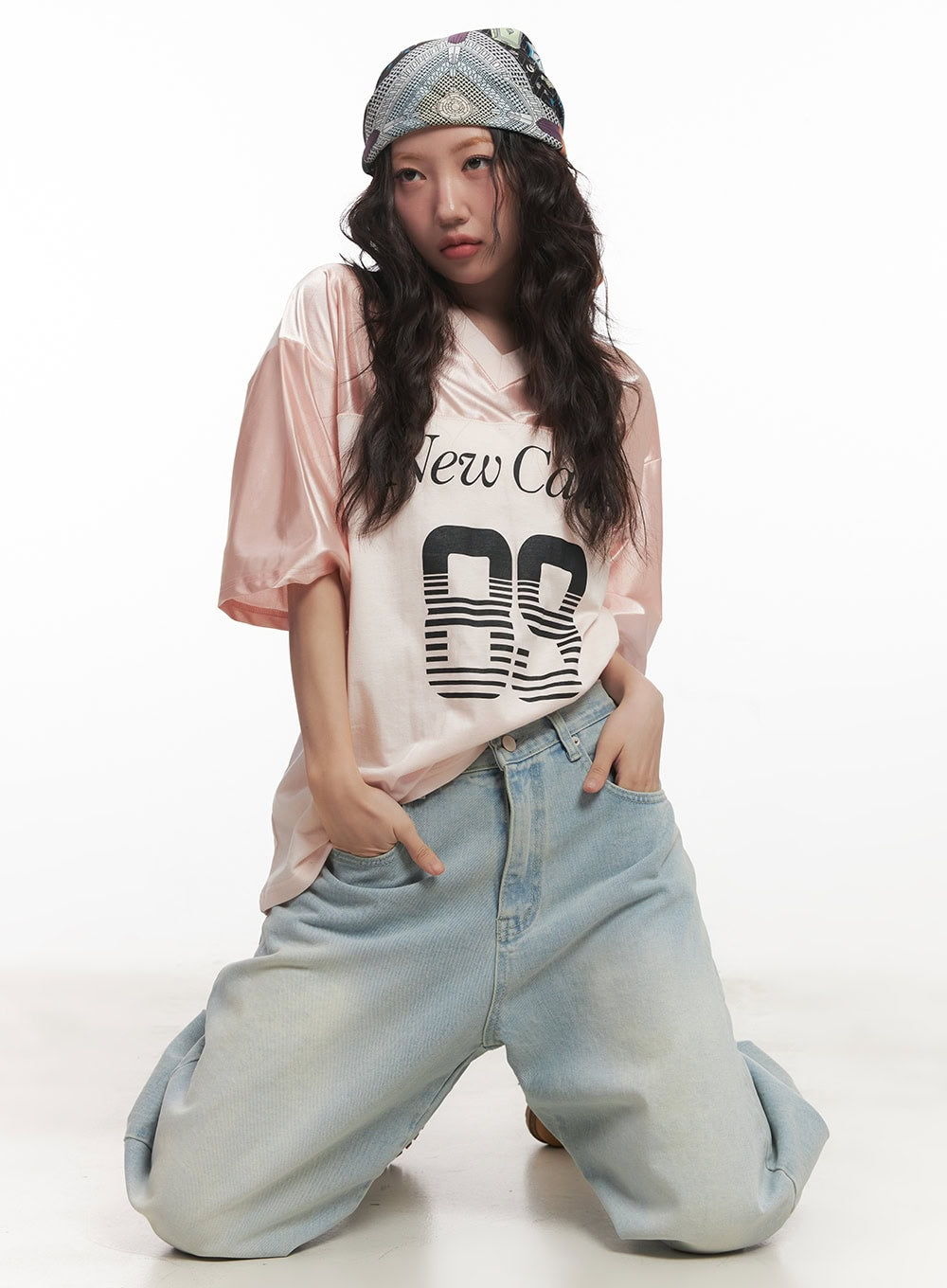 Alia Washed Wide-Leg Jeans CA518 in light blue, dynamic kneeling pose on model, voluminous wide-leg denim bunching at floor, styled with pink graphic tee and patterned headscarf.