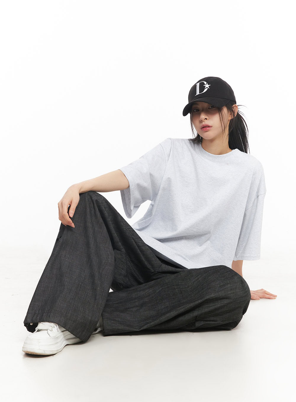 Pintuck Denim Sweatpants IY529 in black, model seated on floor, wide-fit denim fabric draping loosely, paired with white tee, black cap, and white sneakers, showing volume and drape.