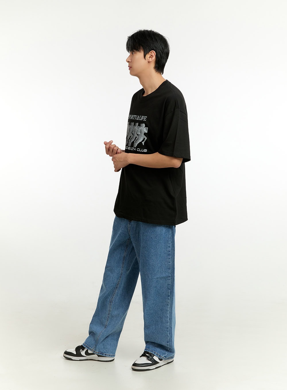 Men's Wide Fit Jeans IL412 in blue, three-quarter side view on model in walking pose, relaxed wide-leg fit, medium wash, paired with black graphic tee and sneakers.