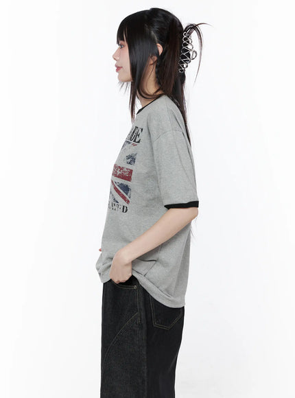 Graphic Short Sleeve Tee CU519 in gray, close side view on model, highlighting drop shoulder fit and black ringer cuff detail, partially tucked over dark denim.