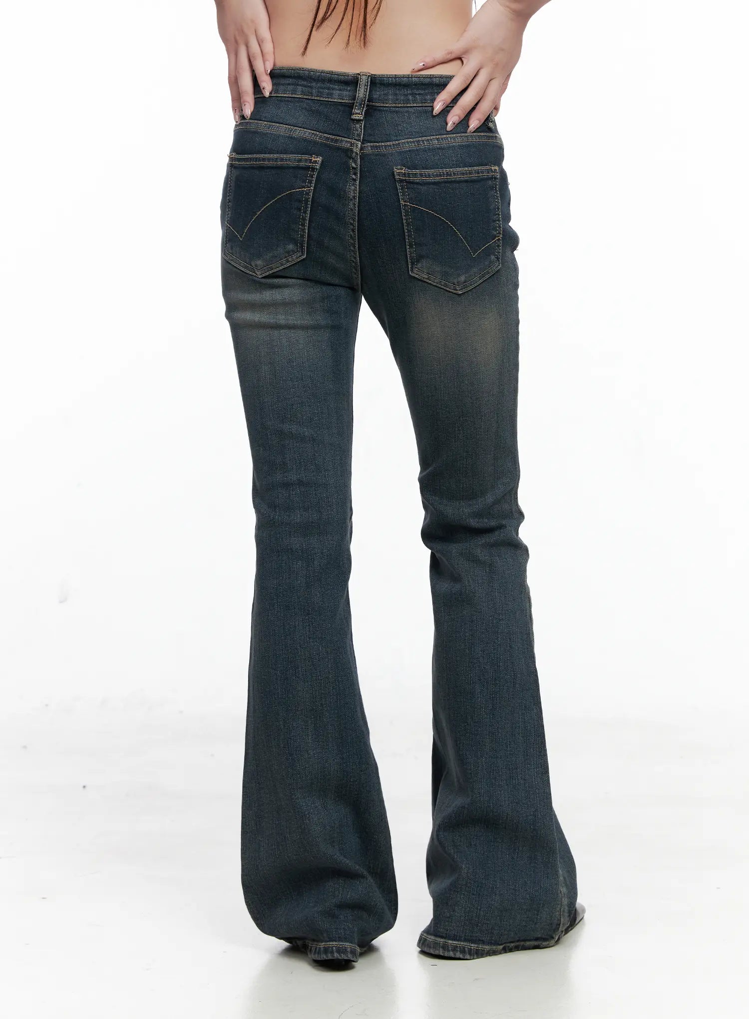 Rosé Washed Bootcut Jeans CO520 in dark blue, back product shot on model, hands on hips, wide curved back pockets with arc stitching, bell-flared hem pooling at floor.