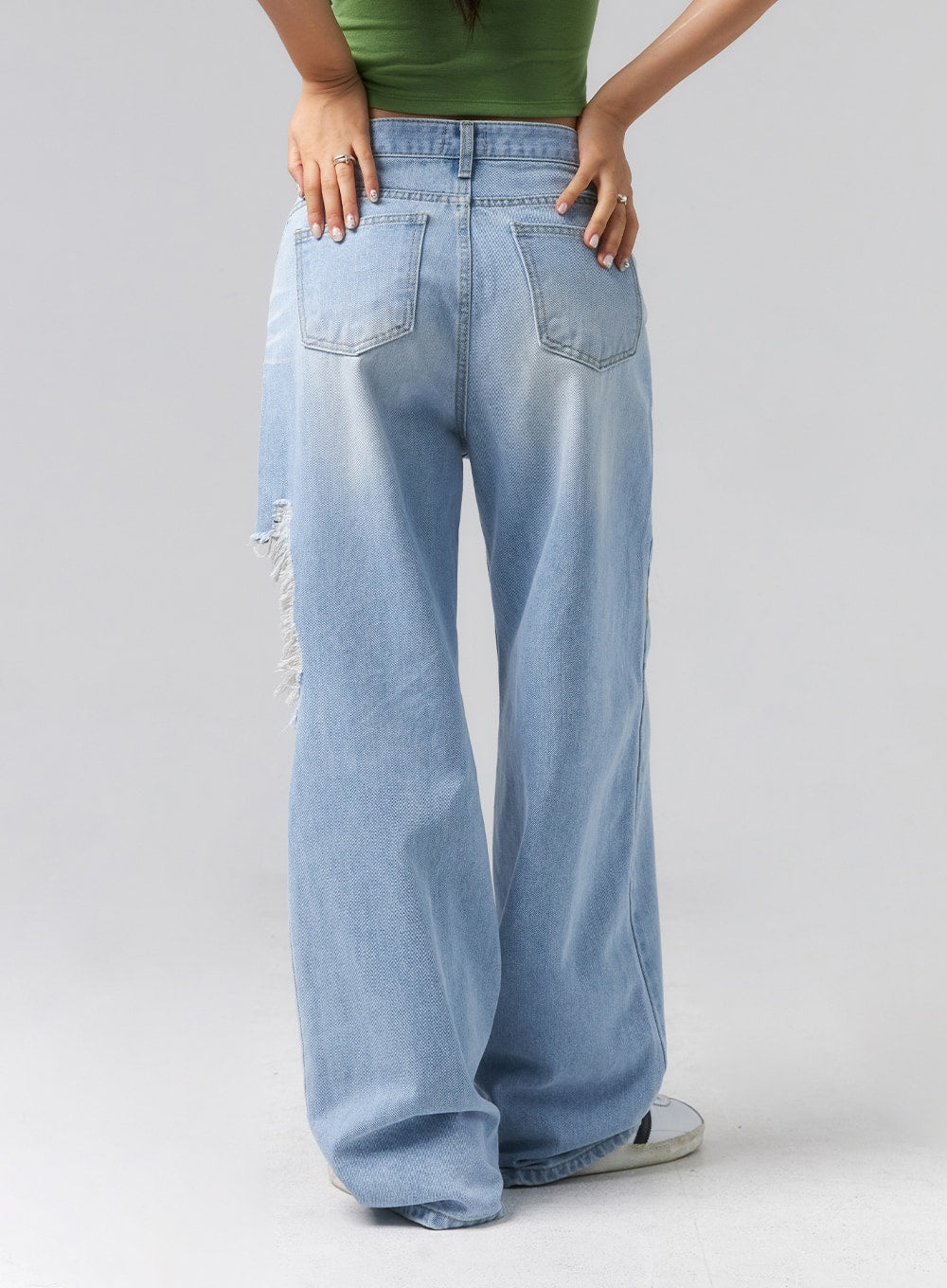 Ripped Side Jeans CL320 in light blue, back view on model, wide-leg cotton denim with dual back pockets and faded wash, frayed destroyed rip visible at side hip, paired with green crop top.