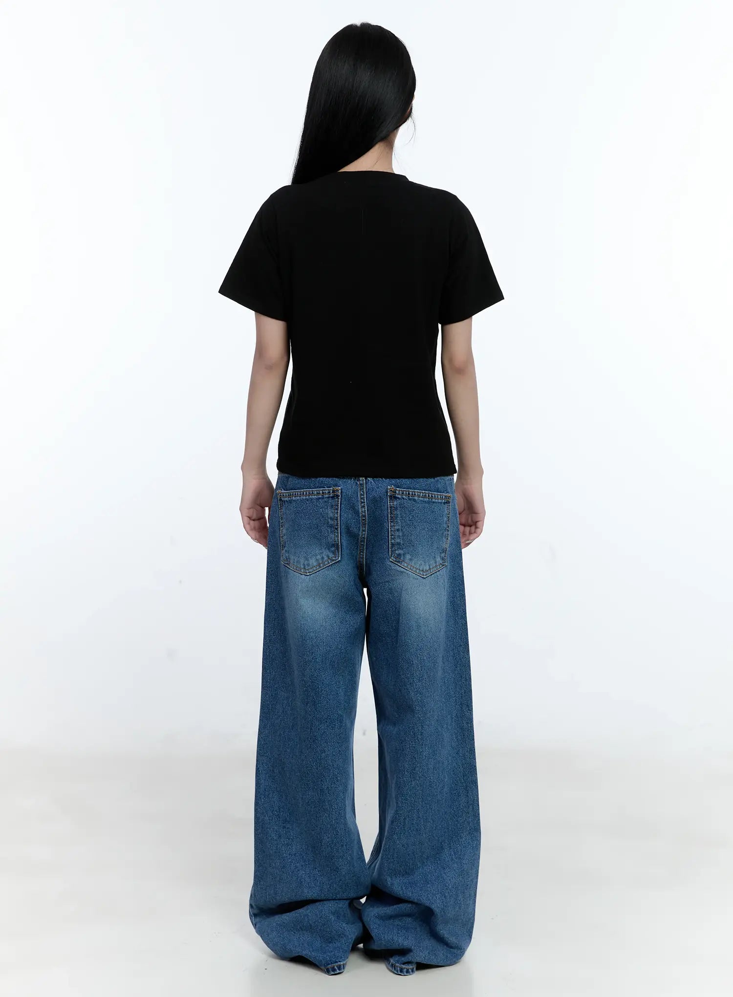Dahye Washed Relaxed-Fit Denim Jeans CL530 in blue, full back view on model, wide-leg silhouette with dual back pockets, washed cotton denim, paired with black crop tee and black heels.
