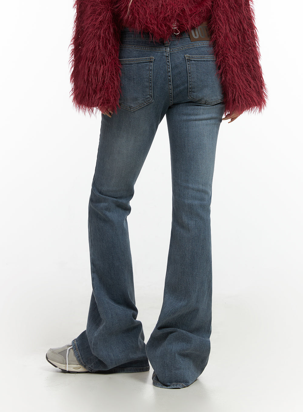 Liv Washed Denim Low Waist Bootcut Jeans CO414 in blue, back close-up on model, rear pockets and bootcut flare hem detail, washed blue denim, styled with red fluffy outerwear and sneakers.