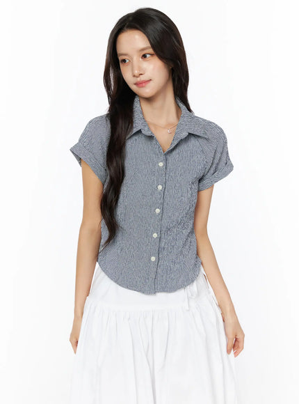 Gingham Button-Up Short Sleeve Blouse CU522 in navy, front three-quarter view on model, cropped fit with point collar and pearl buttons, cuffed short sleeves, white skirt.