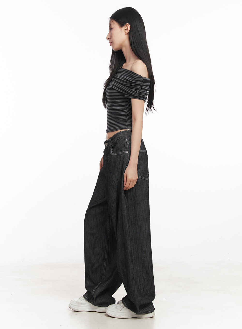 Lilli Wide-Leg Baggy Jeans IY516 in Black, side view on model, silhouette shows dramatic balloon-leg volume, low rise waist and pooling hem, paired with striped crop top and white sneakers.