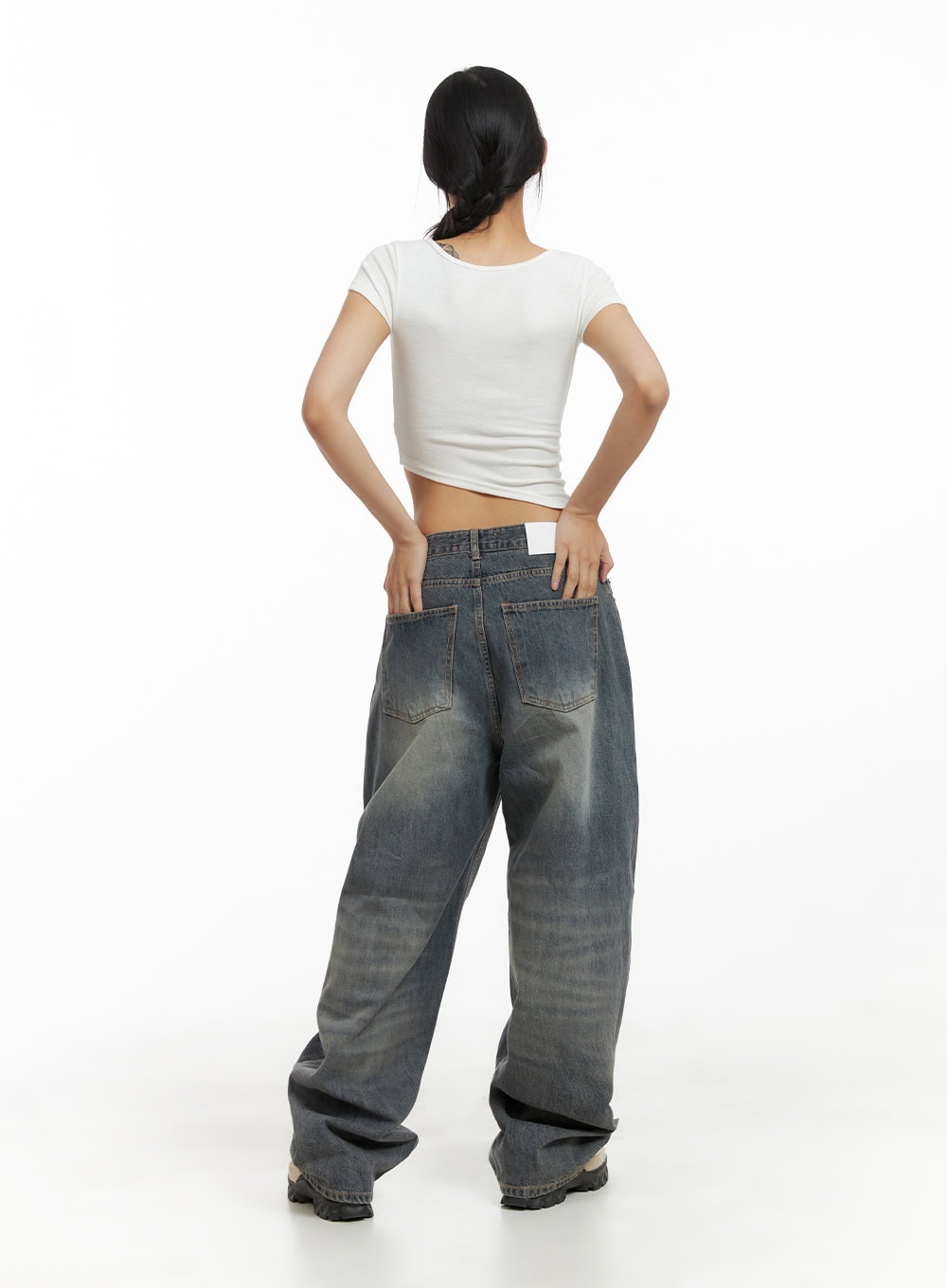 Vintage Washed Baggy Jeans CA424 in blue, full-body back view on model, wide-fit vintage-washed denim with brand label at waist, pooling hem, styled with white crop top and chunky sneakers.