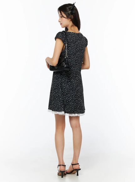 Floral Lace Trim Mini Dress CU522 in black, full back view on model holding shoulder bag, showing back bodice, floral print, white lace hem trim, cap sleeves, strappy heels.