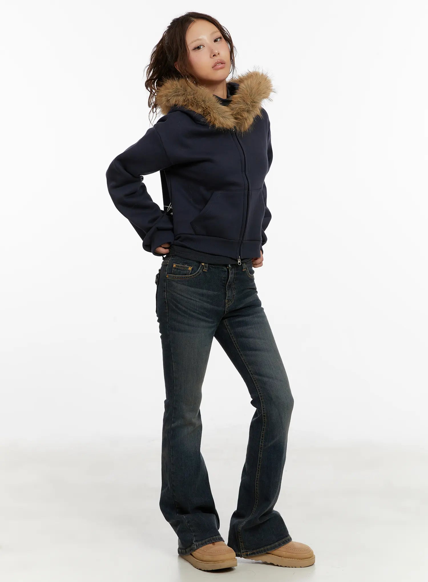 Kai Vintage Washed Flare Jeans CD515 in dark indigo, three-quarter front side view on model posing with hand on hip, flare leg visible, styled with navy fur-hood zip hoodie and UGG boots.
