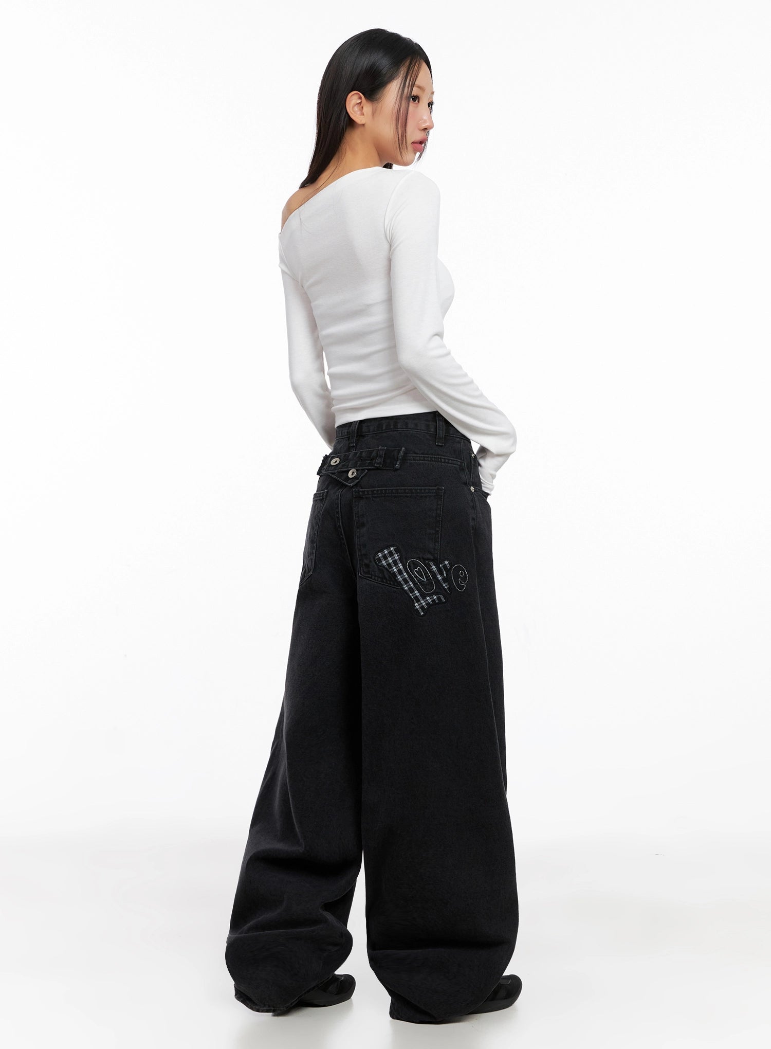 Sunwoo Embroidered Wide Leg Jeans IG528 in black, rear full-length view on model, gingham patch 'love' embroidery on back pocket visible, ultra-wide leg cotton denim with side-buckle waist detail.