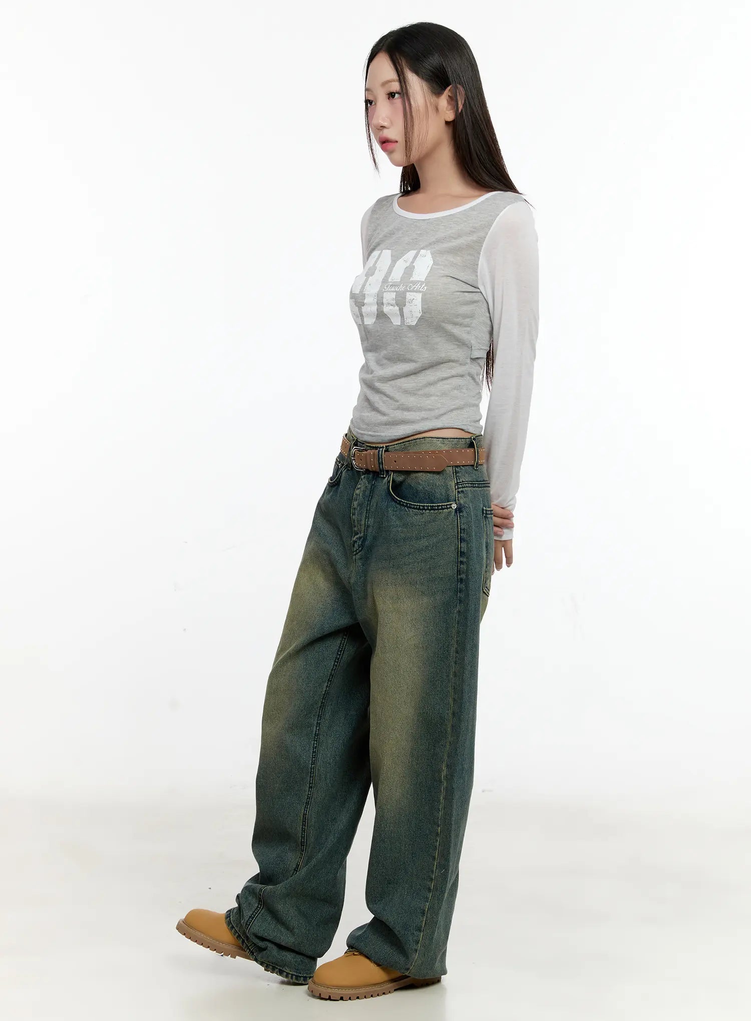 Sooyoung Baggy Vintage Wash Jeans CL531 in dark blue, three-quarter side view on model, wide-leg baggy fit with vintage green-yellow wash, belted, paired with graphic crop top and tan boots.