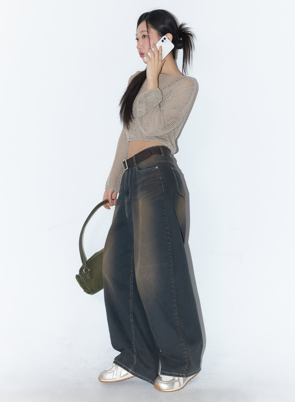 Bethany Vintage Washed Baggy Jeans IA524 in dark brown washed denim, side profile view on model holding green bag and phone, wide-fit silhouette with brown fade wash, belted, with silver sneakers.