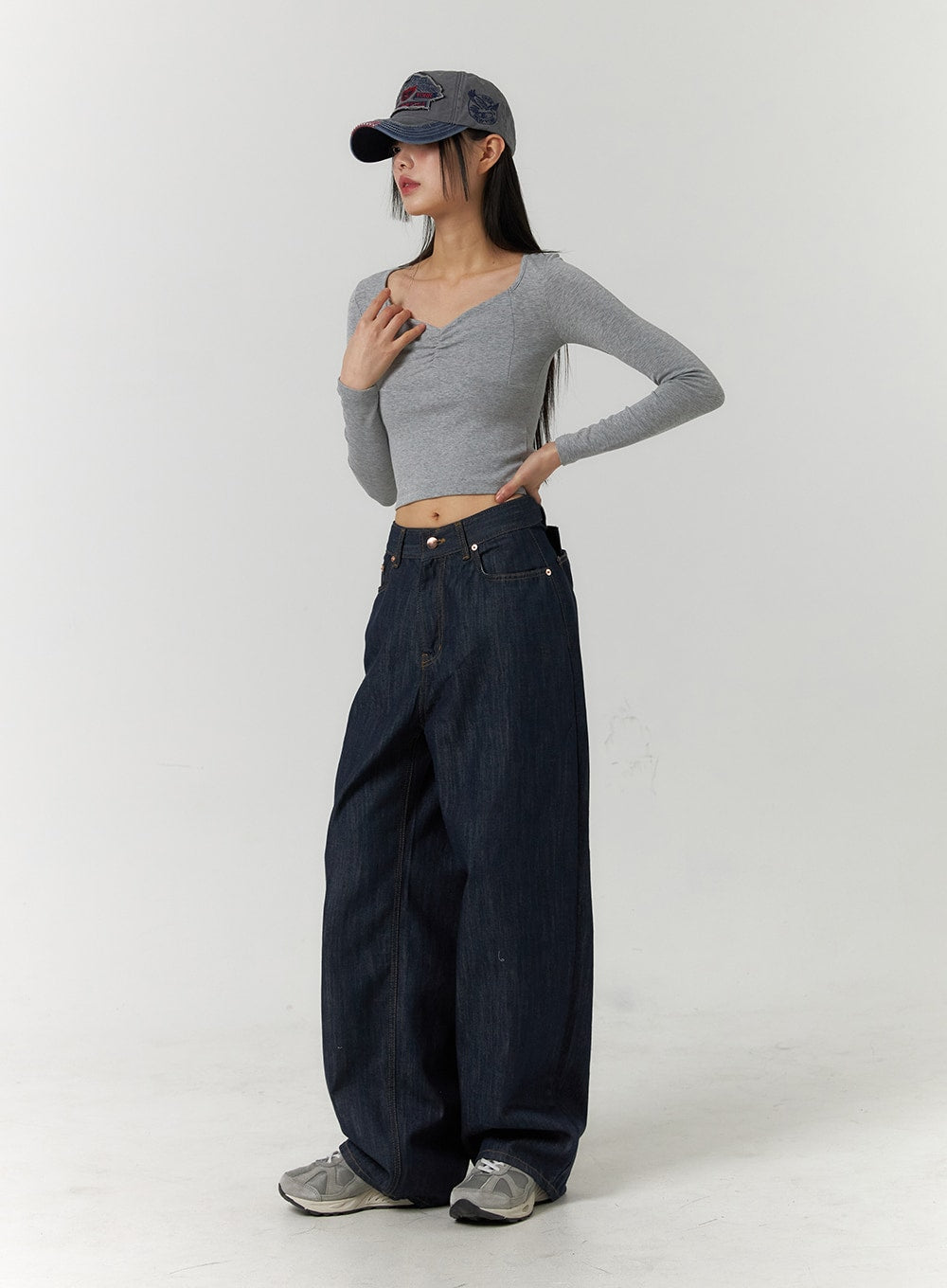 Back Button Wide Leg Jeans CF407 in blue, three-quarter front view on model with hand on chest, low-rise wide-leg dark indigo denim, styled with grey crop top and denim cap.