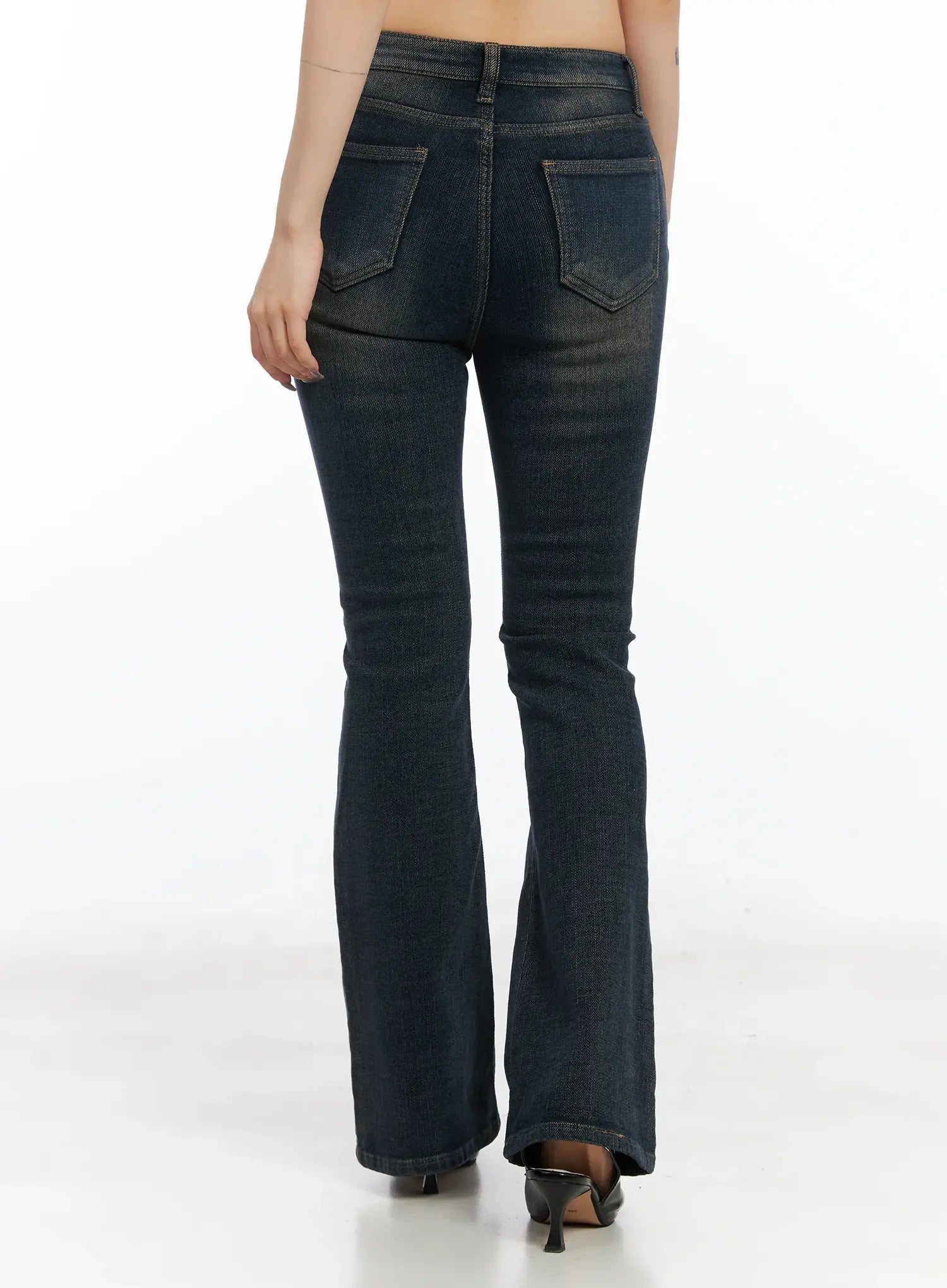 Jordyn High-Waist Bootcut Jeans CD502 in dark washed indigo, back view on model, curved back pockets with topstitching, fitted seat and thigh, flared bootcut hem, worn with black kitten-heel mules.