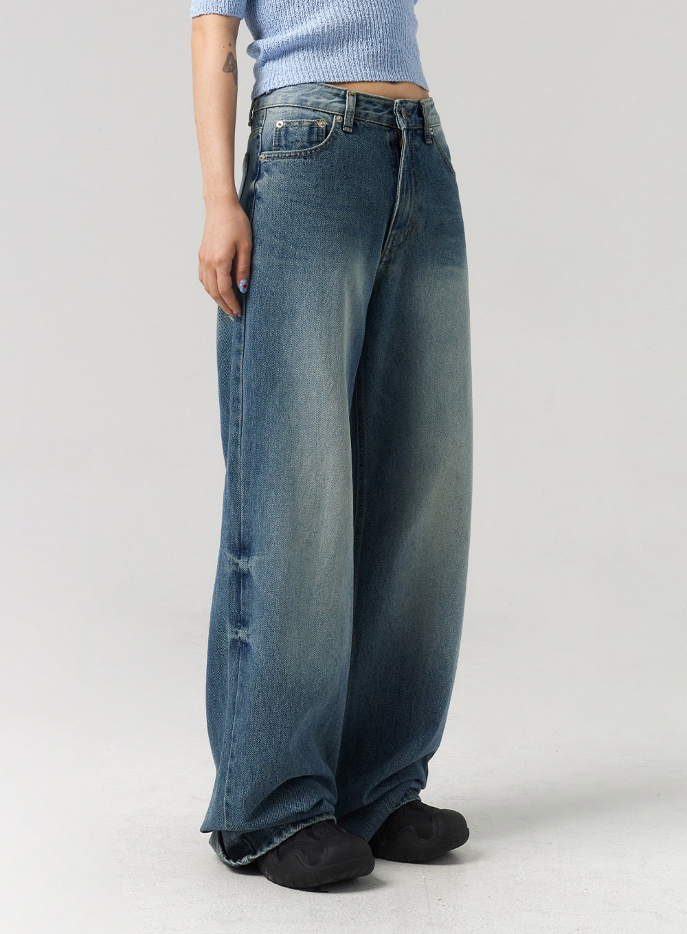 Mid-Wash Baggy Jeans CL312 in mid-wash blue, side view close-up on model, voluminous wide leg silhouette with heavy fade on outer thigh, raw hem pooling over shoes.